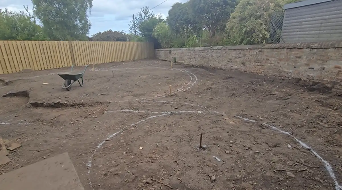 Cleared plot of bare earth with new timber fencing installed and the curved layout marked out in the soil