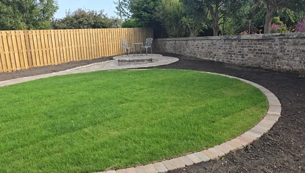 Completed curved lawn edged with a brick border beside the new pond surround and timber fence