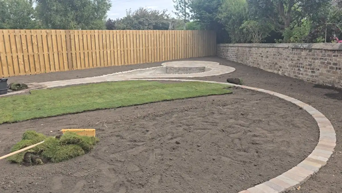 First rolls of turf being laid over fresh topsoil inside the curved brick lawn border